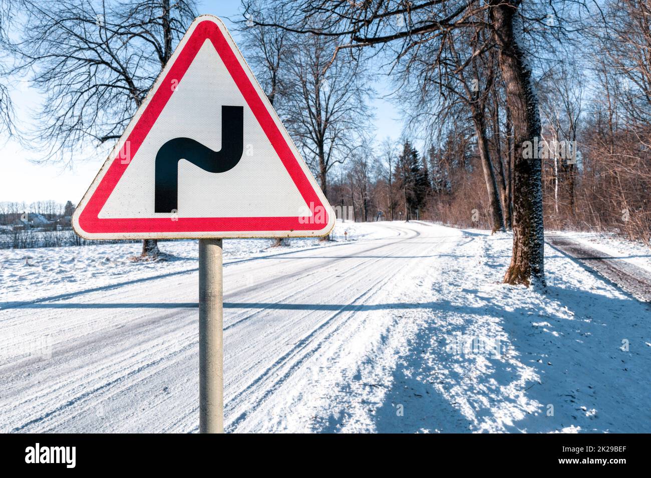 Warning road sign indicating a double bend in wintry conditions Stock Photo