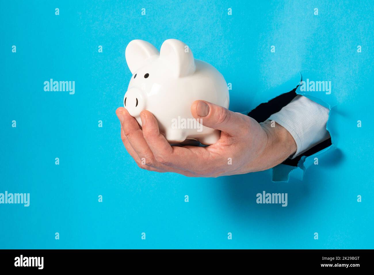 Hand with a white piggy bank through a paper hole Stock Photo Alamy