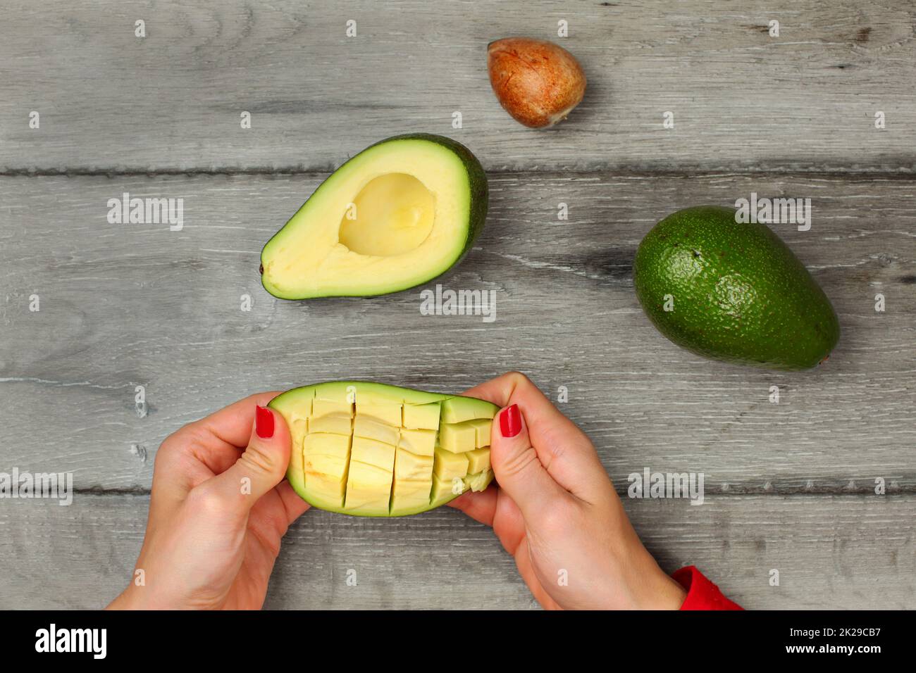 Tabletop view, young woman hands holding avocado with cuts, getting out the pulp. Stock Photo