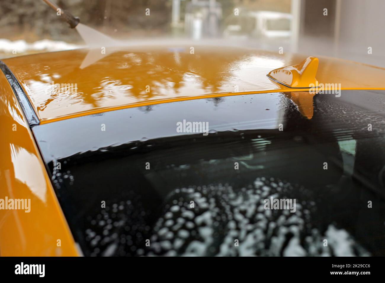 Top of yellow car washed in carwash, water flowing on roof and small antenna. Stock Photo