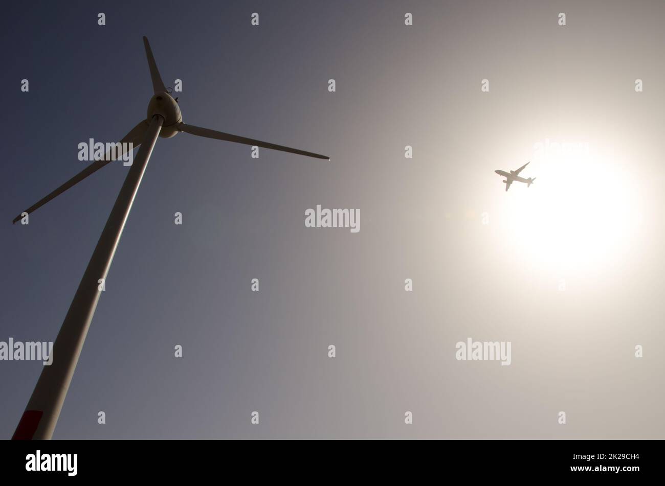 Airplane and wind turbine against the light. Stock Photo