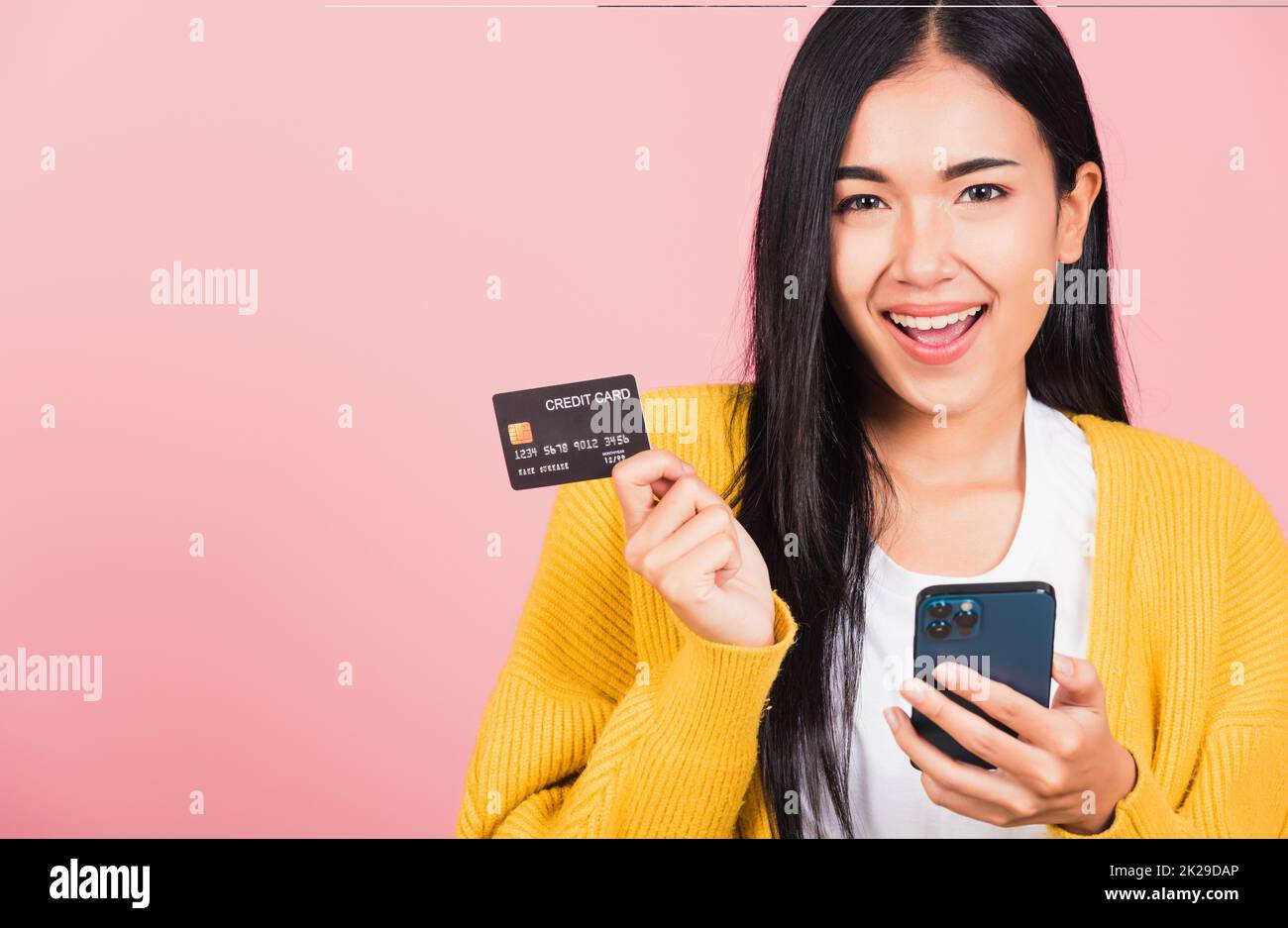 Happy Asian portrait beautiful cute young woman excited smiling hold mobile phone and plastic debit credit bank card, studio shot isolated on pink background, female using smartphone online shopping Stock Photo