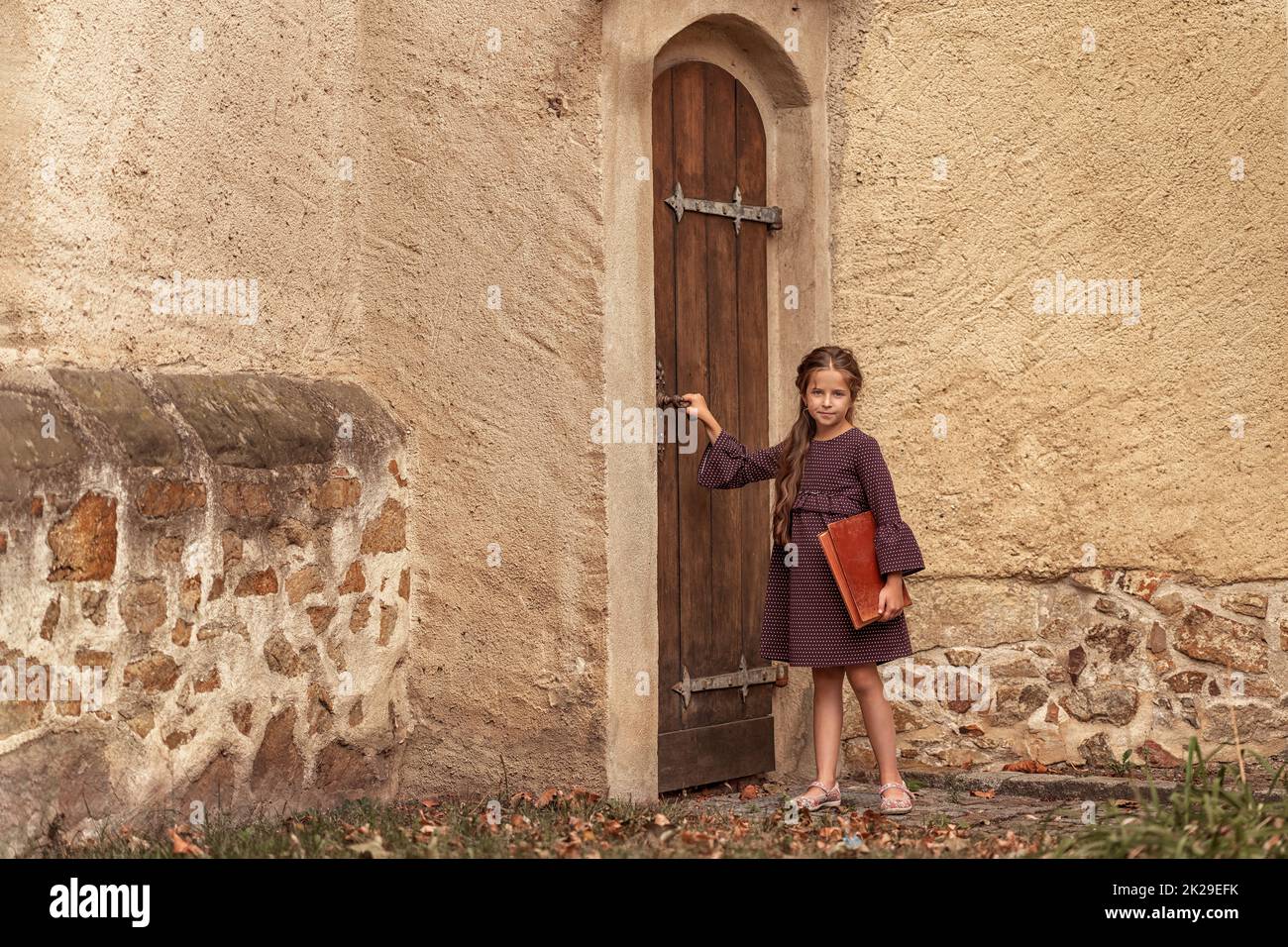 Portrait of a beautiful little girl with an old encyclopedia in her hands in the courtyard of the house. Stock Photo