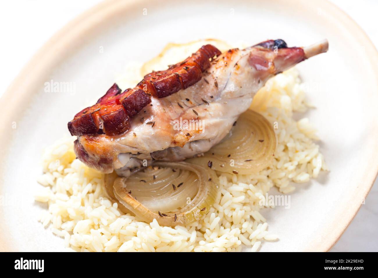 rabbit leg baked with bacon and onion served with rice Stock Photo Alamy
