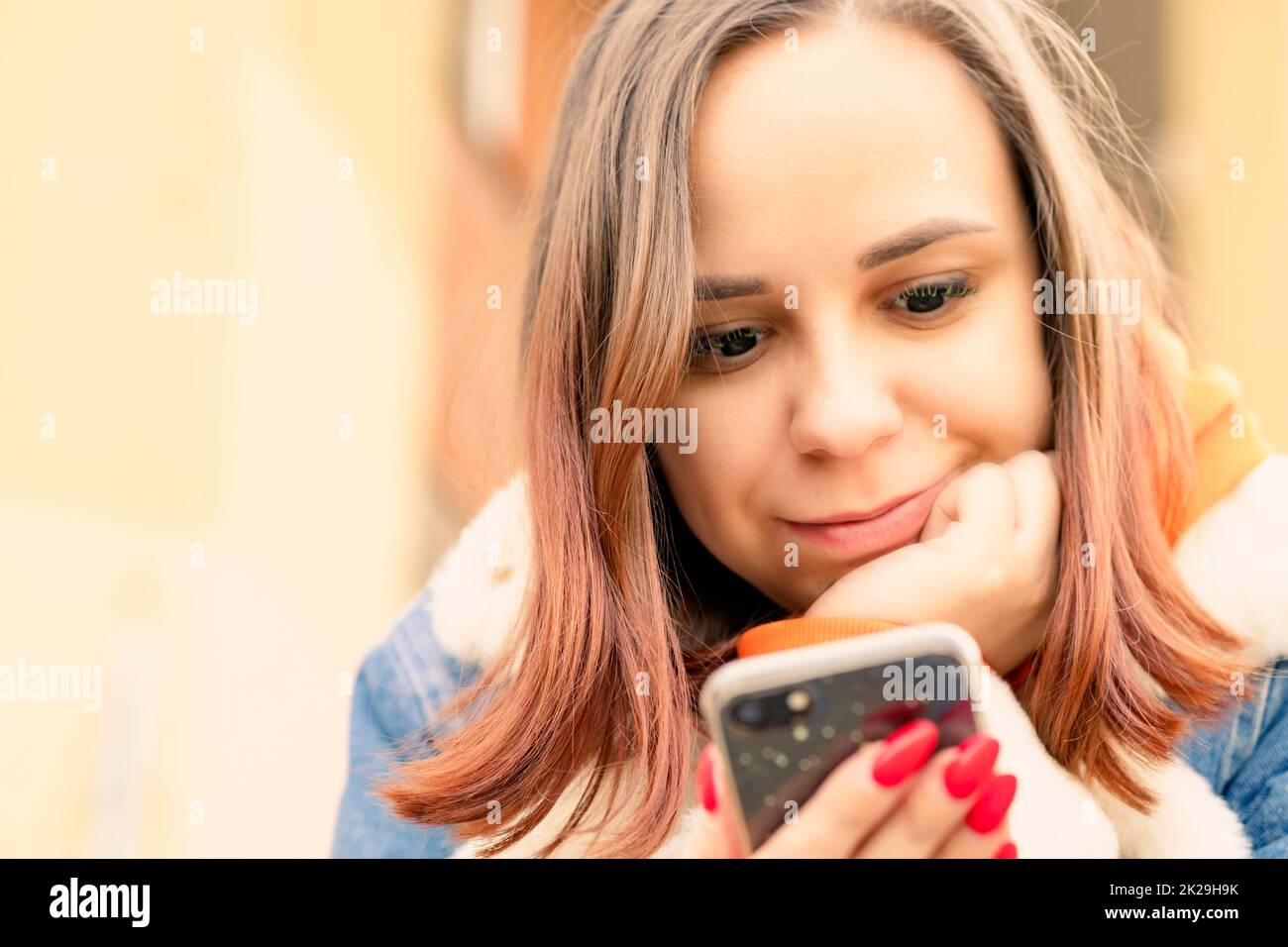 Portrait of young woman browsing mobile phone, sitting, leaning on hand. Close up Stock Photo