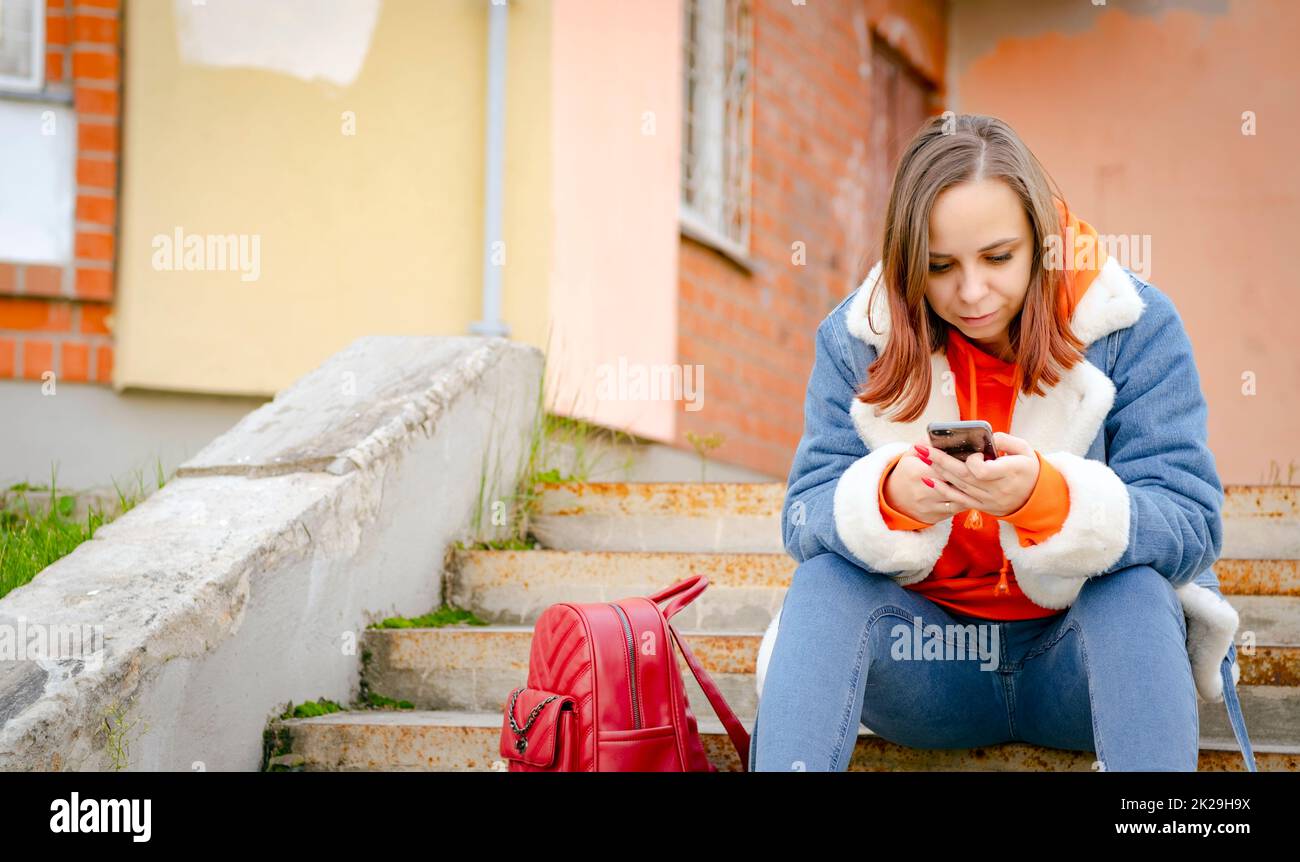 Young woman with mobile phone sitting on steps on street Stock Photo