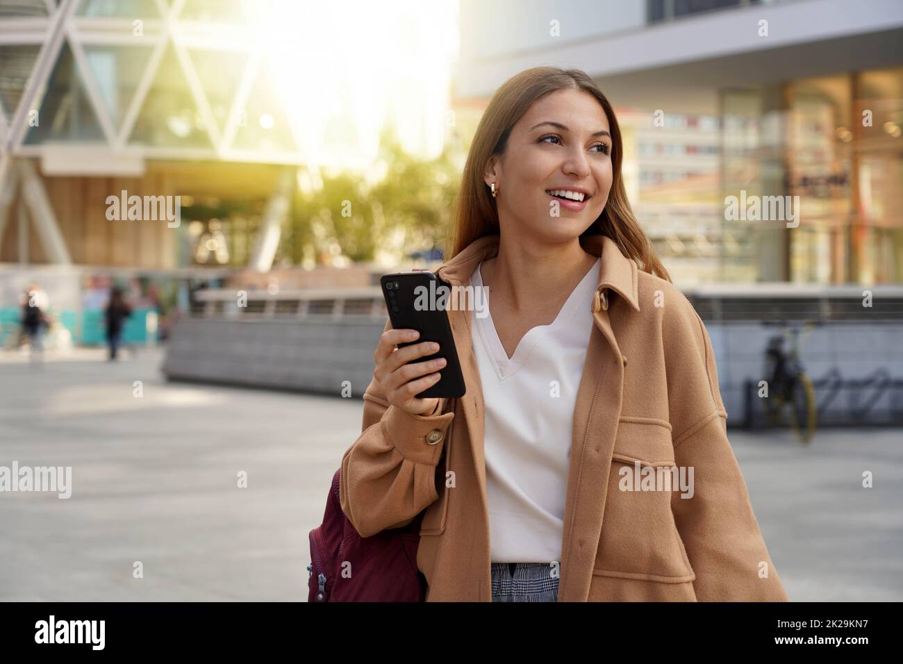 Beautiful woman walking in modern city using mobile phone looking side at sunset time Stock Photo