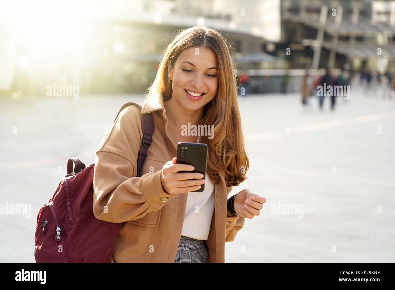 Beautiful smiling student girl using cellphone walking in city street Stock Photo