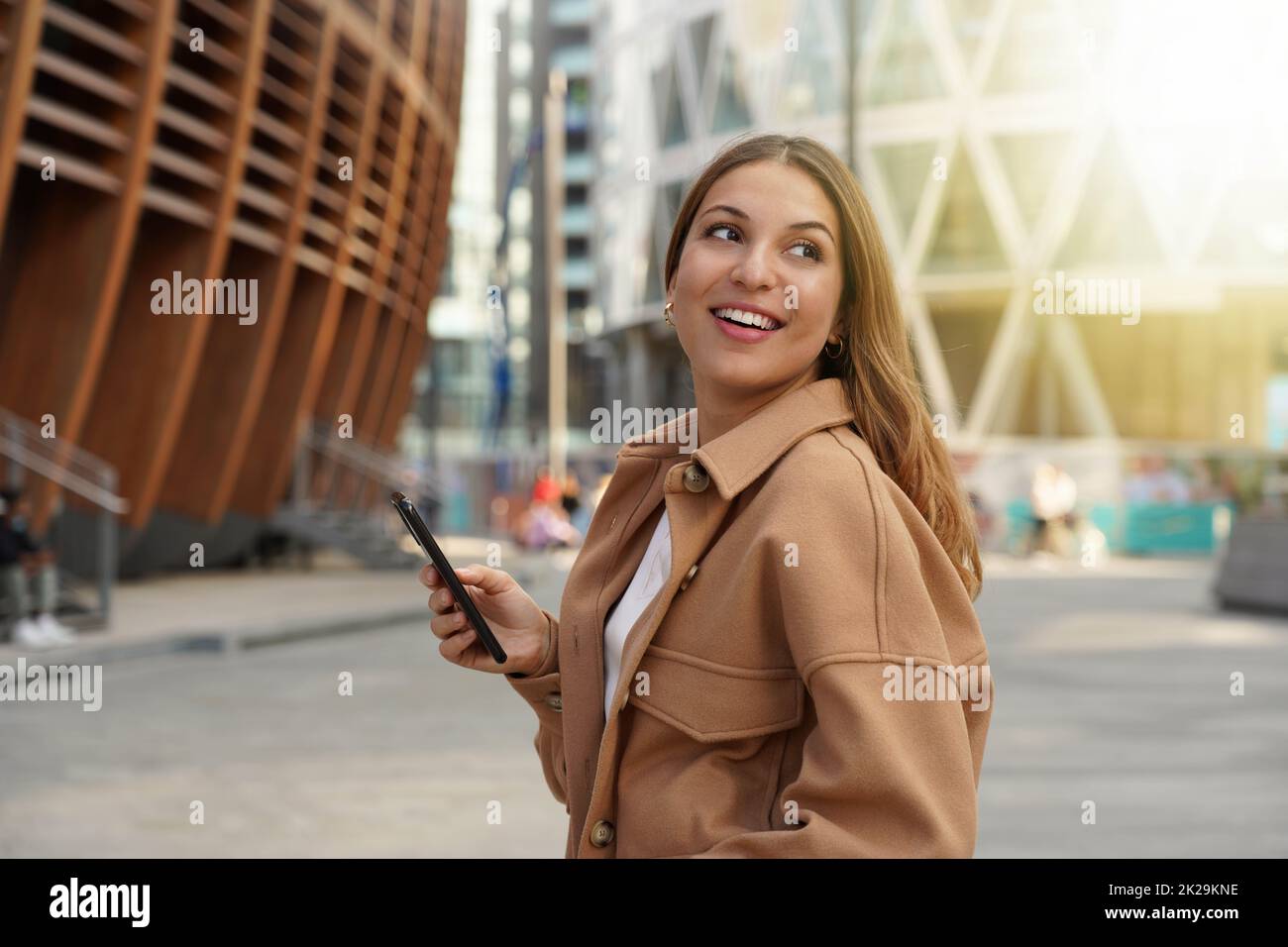 Beautiful woman walking in modern city using mobile phone looking side at sunset time Stock Photo