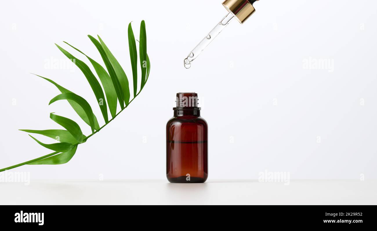 essential oil falling from the amber glass dropper. Blue bottle of cosmetic oil with a pipette, white background Stock Photo