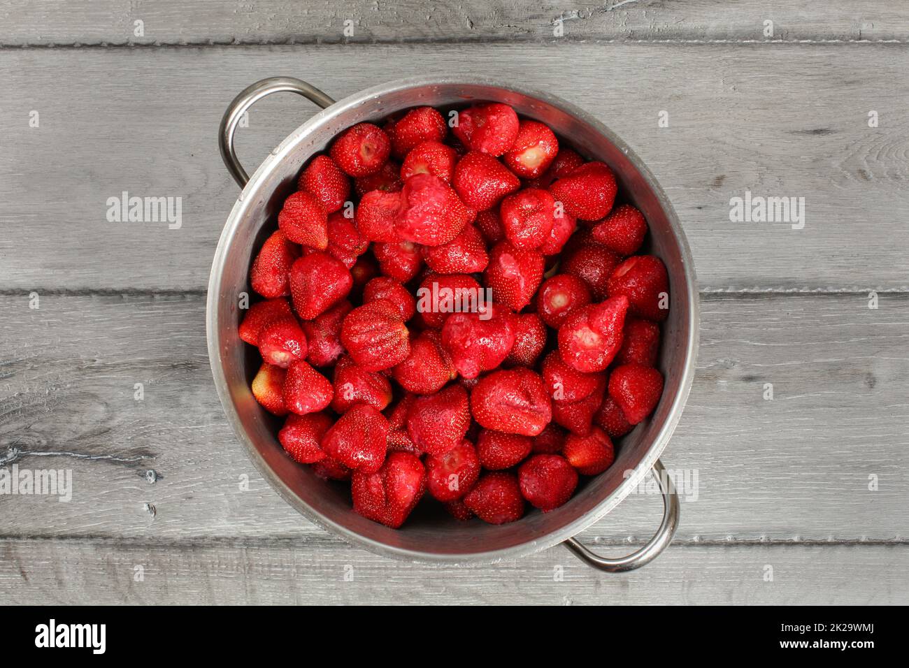 Tabletop view, steel pot full of strawberries with leaves removed. Homemade strawberry jam preparation. Stock Photo