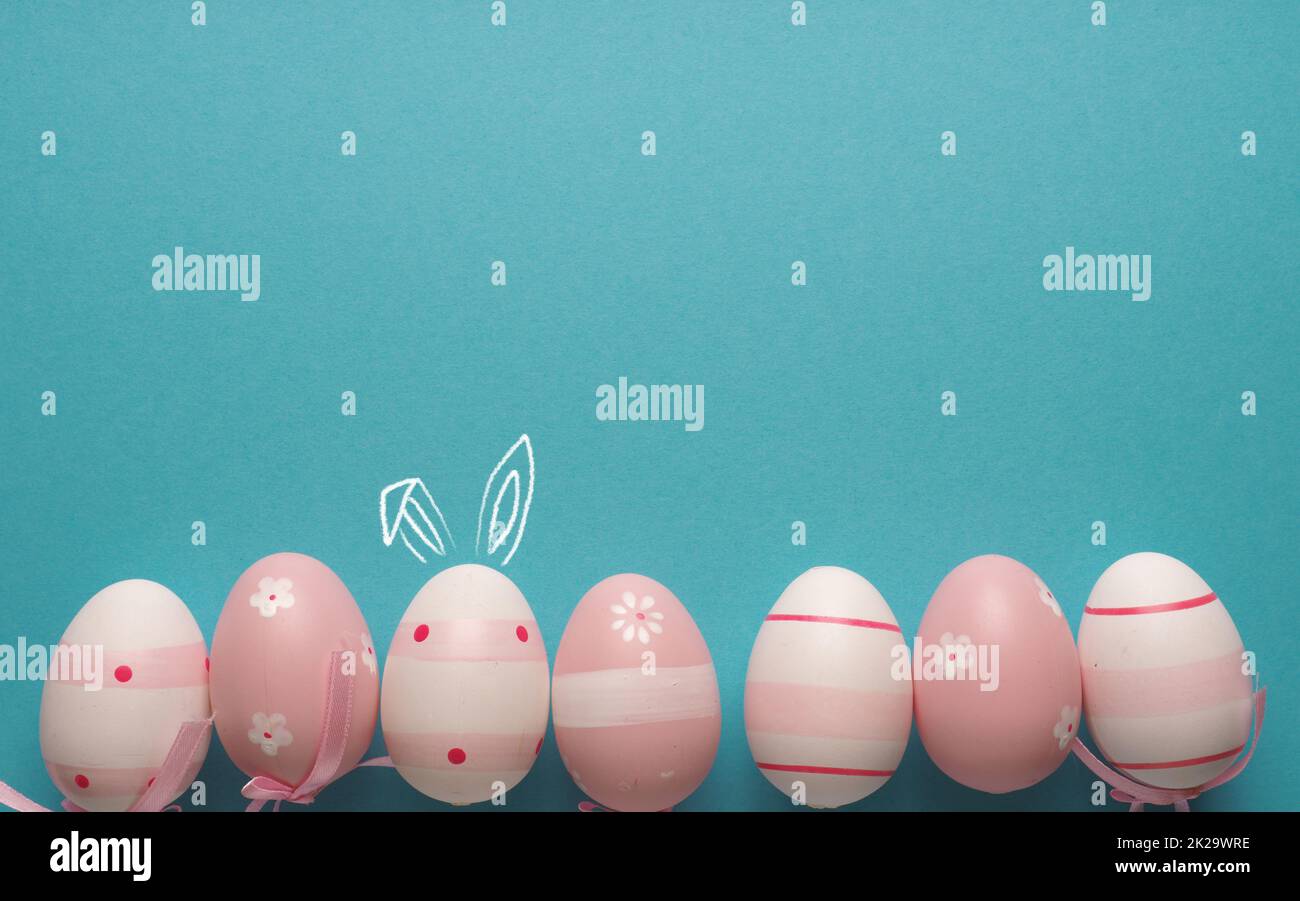 Pink Easter eggs in a row on blue, one with bunny ears Stock Photo