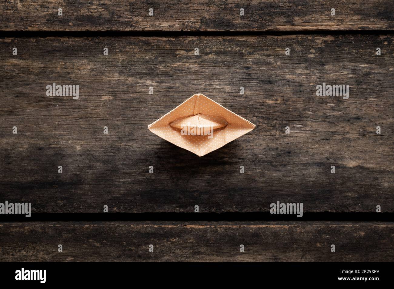 Top view of an origami boat made of polka dot paper placed on rustic wooden boards. Stock Photo