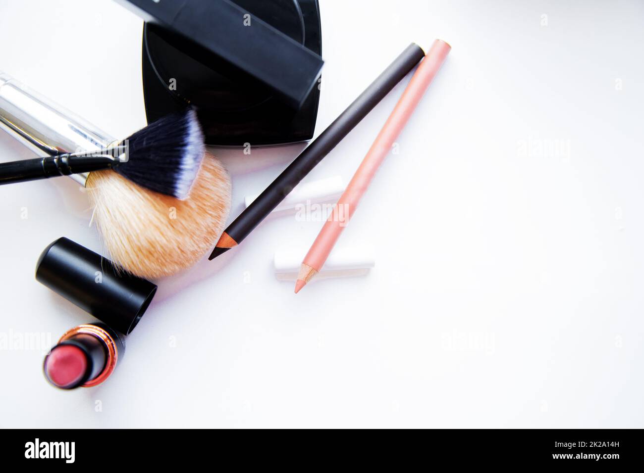 Two pencils for eyes and lips, lipstick, brushes and blush lie together on a white background with a place for text Stock Photo