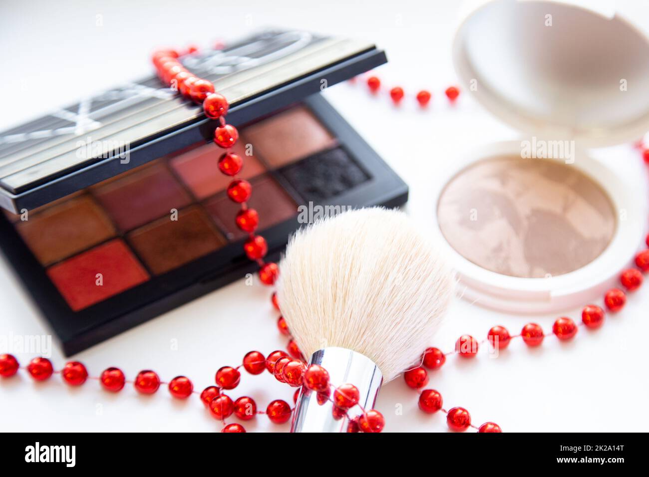 The white face powder and bronzer, black packaging with a eyeshadow brush and lying on a white background, braid with red beads closeup Stock Photo