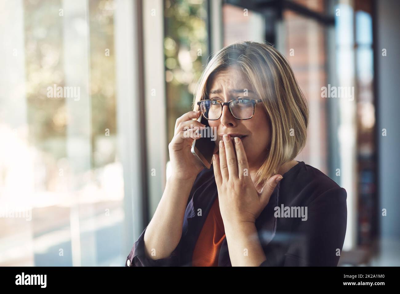 In that moment, life changed forever. Shot of a young woman looking distraught while talking on a mobile phone in a modern office. Stock Photo
