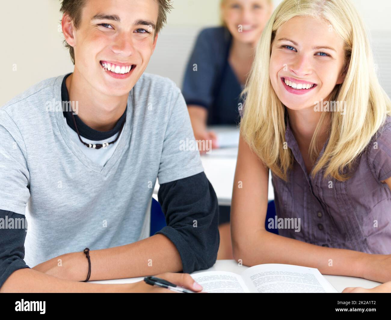 Young boy and girl sitting together in class. Closeup of happy young boys and girls sitting together in class with notes. Stock Photo