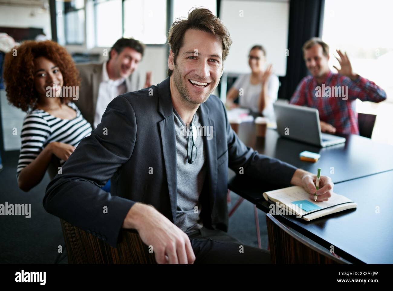 In the company of great minds. Portrait of an office worker sitting at a boardroom table with colleagues in the background. Stock Photo