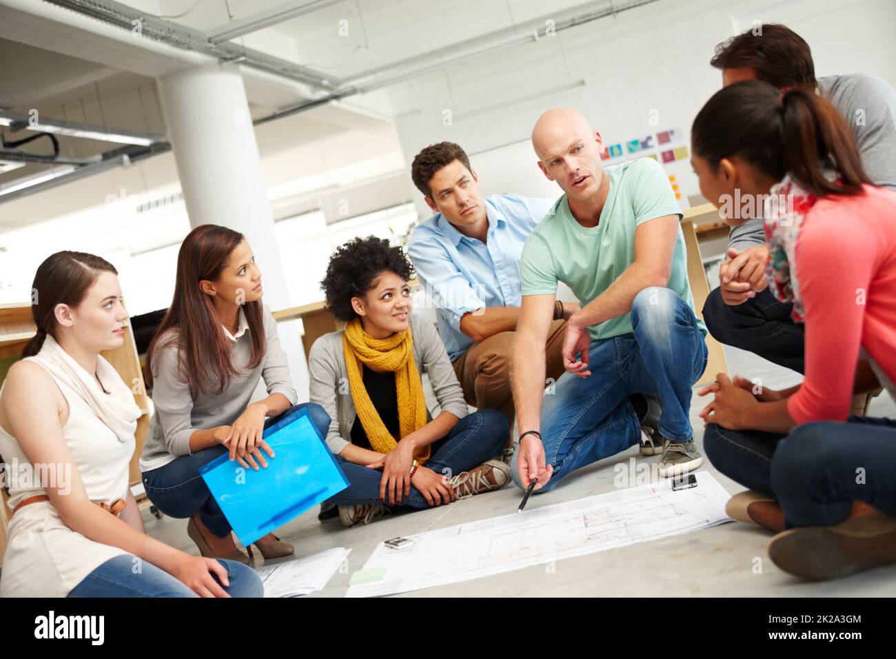 Dynamic designers. A group of multi-ethnic creatives huddled together and listening to the presentation of a plan. Stock Photo