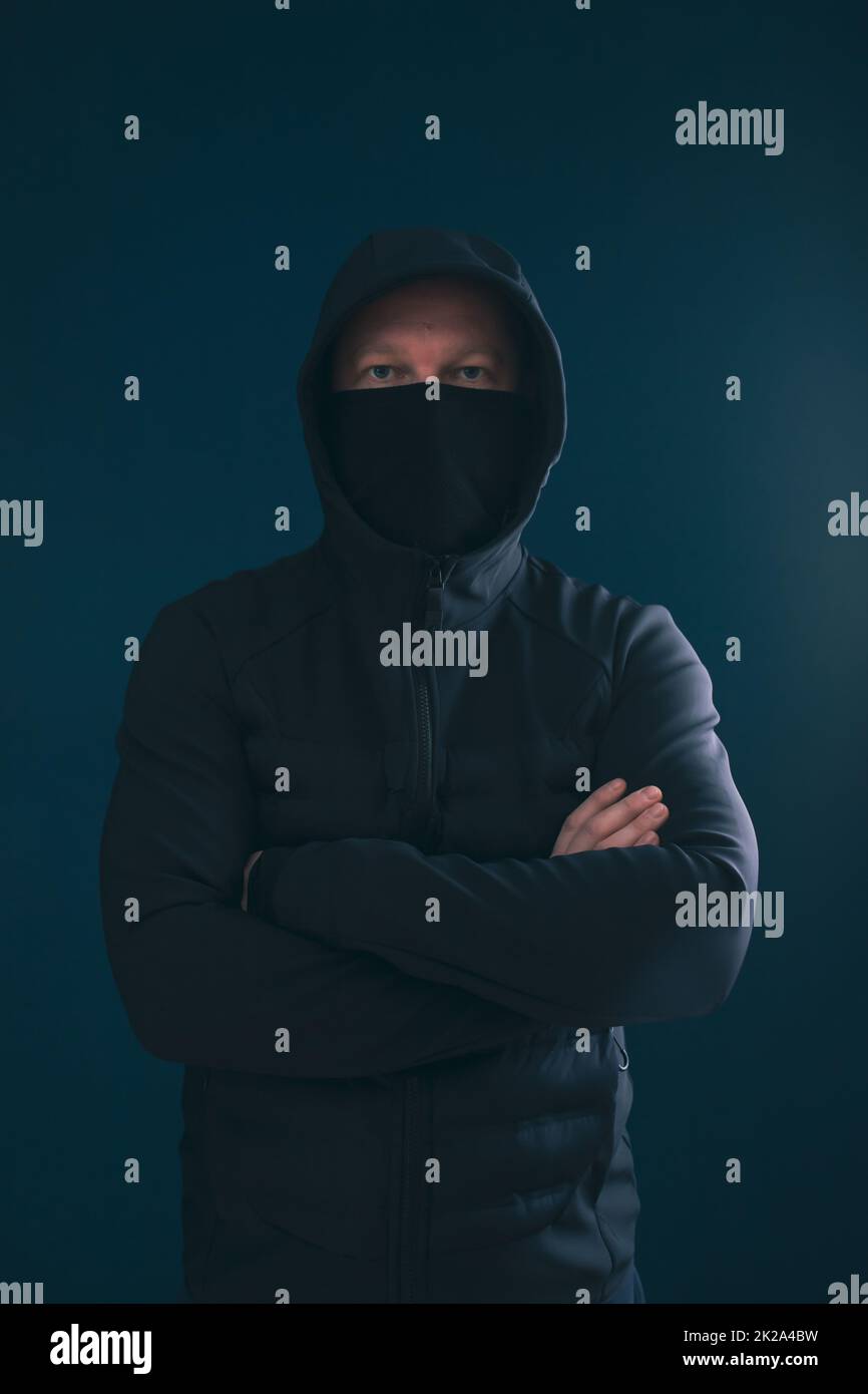 Mystery man with hidden face in a hood in the dark. Stock Photo