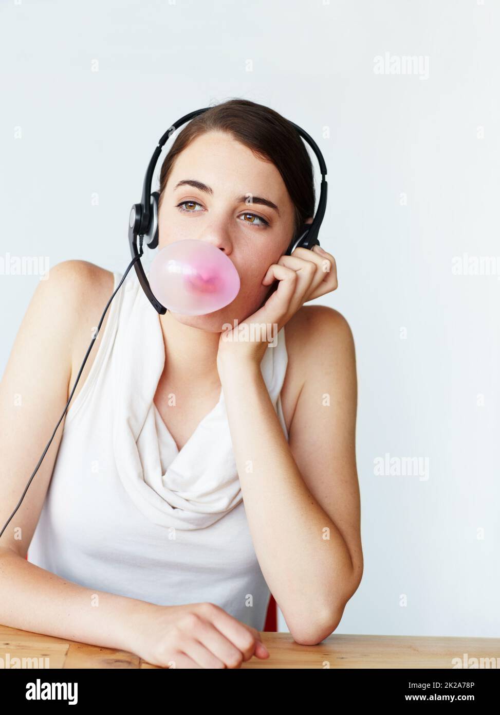 Bubbles of boredom. A beautiful young customer service representative sitting at a table and blowing a bubble while chewing bubblegum. Stock Photo