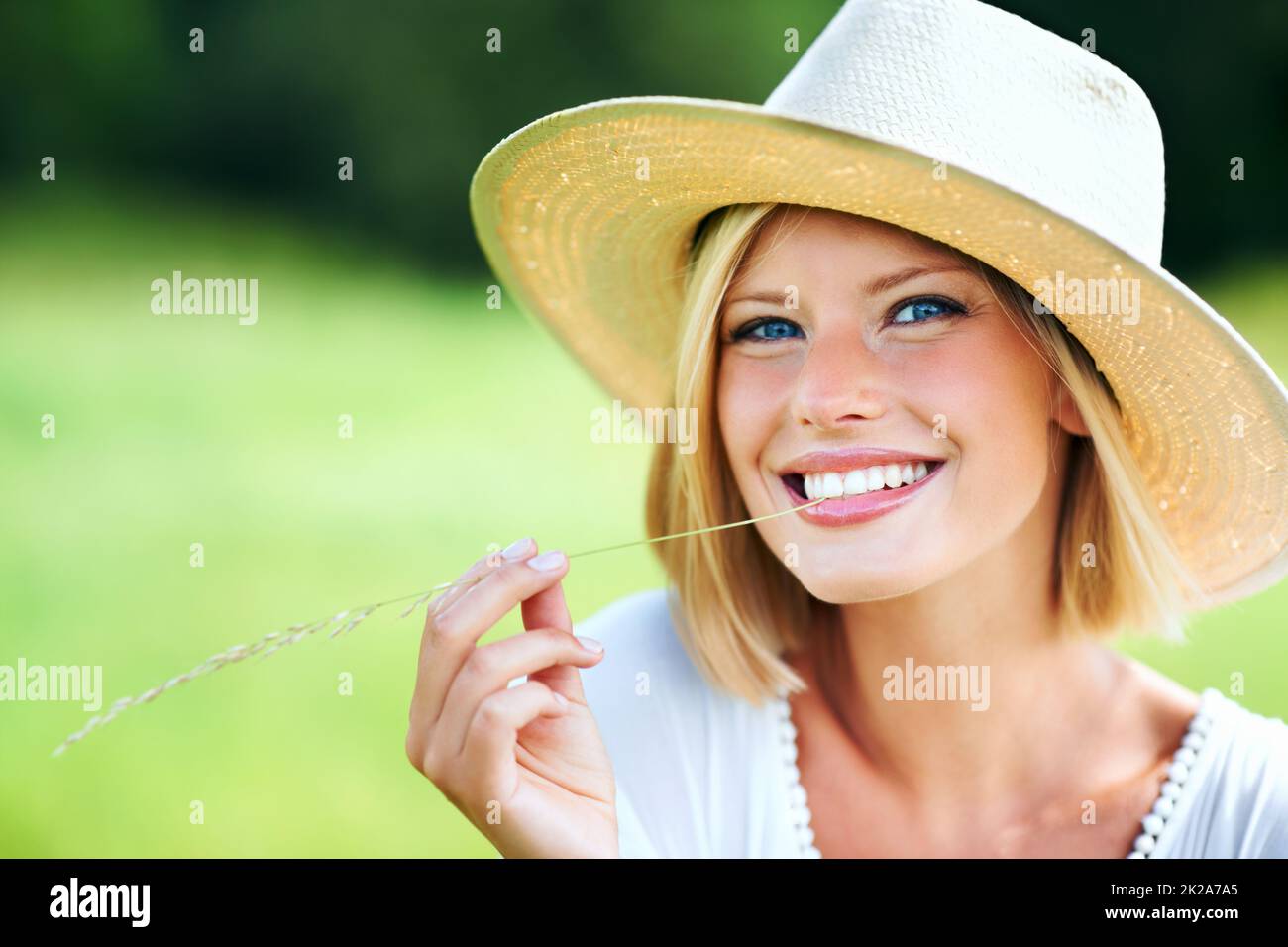 Countryside cutie. Cute young woman smiling while wearing a hat and chewing a wheat stalk. Stock Photo