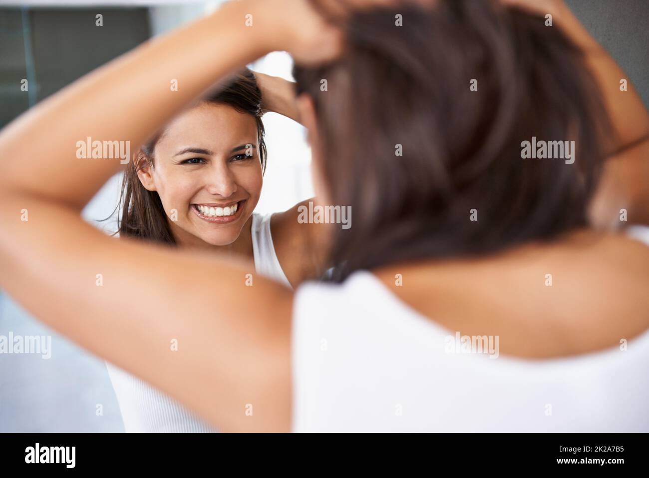 Getting ready is half the funof going out. A cropped shot of a happy young woman deciding on a hair style in front of her bathroom mirror. Stock Photo
