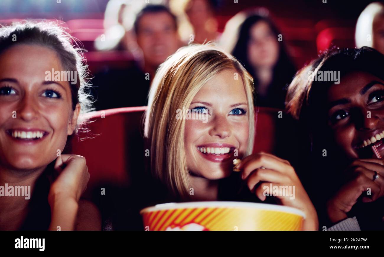 Girls night. Three friends laughing during a movie while eating popcorn. Stock Photo