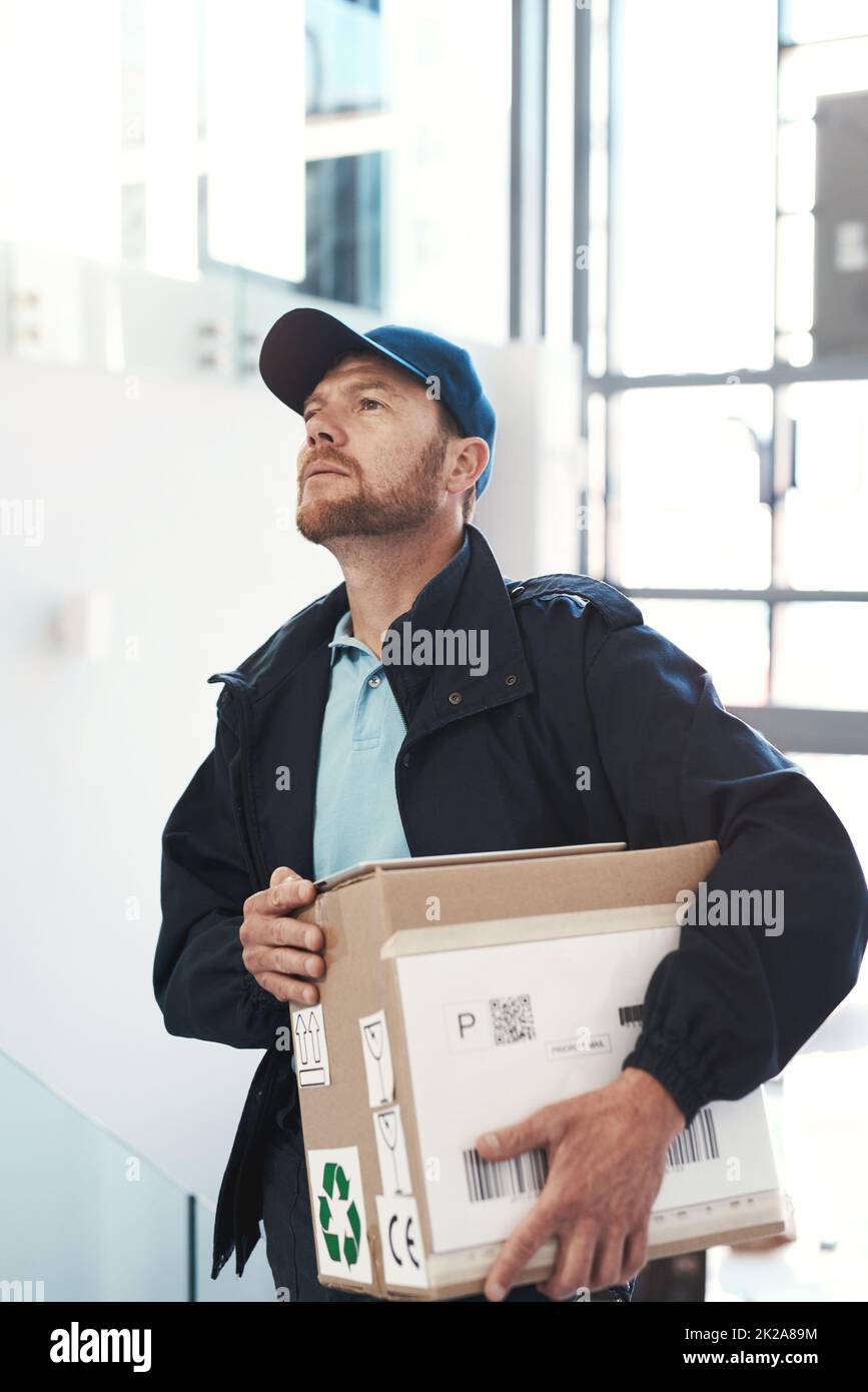 Hes on route to make a delivery. Shot of a handsome delivery man heading up a flight of stairs with a customers order. Stock Photo