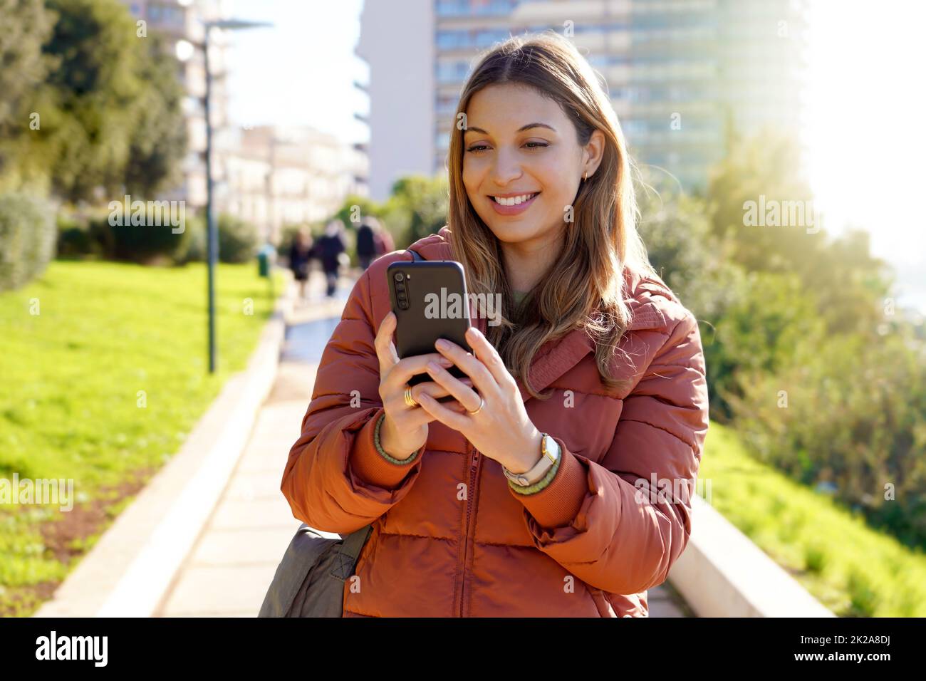 Young woman outdoor using smartphone wearing winter coat watching video streaming Stock Photo
