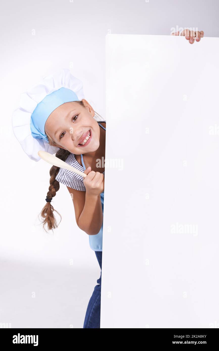 I love cooking.. Young girl wearing a chefs hat and holding a blank board reserved for copyspace. Stock Photo