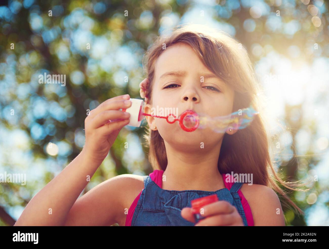 Keep calm and blow bubbles. Shot of a cute young girl blowing bubbles outside. Stock Photo