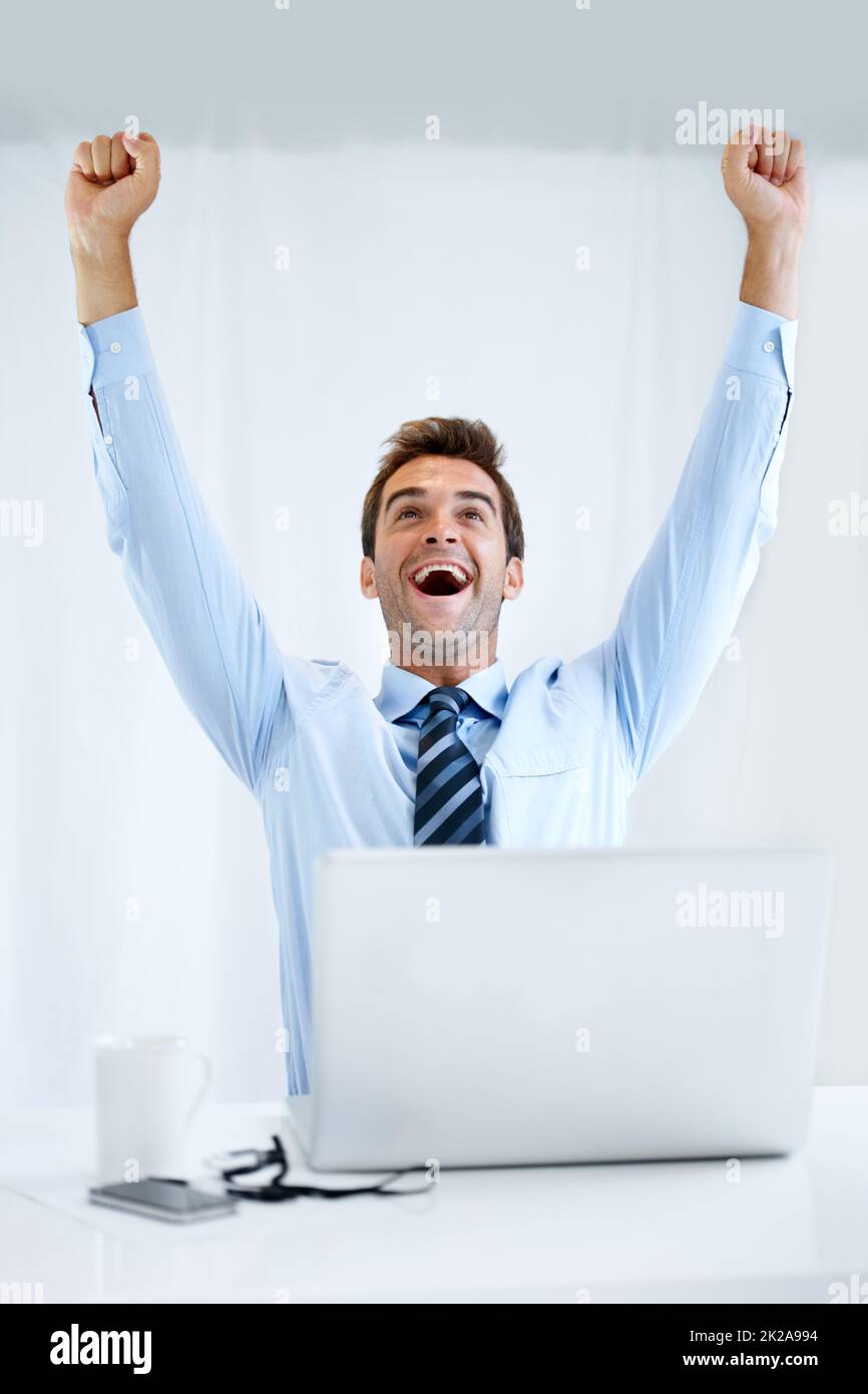 He never thought hed make the deadline... But he did. A businessman sitting at his desk with his computer in front of him and cheering with his arms raised above his head. Stock Photo