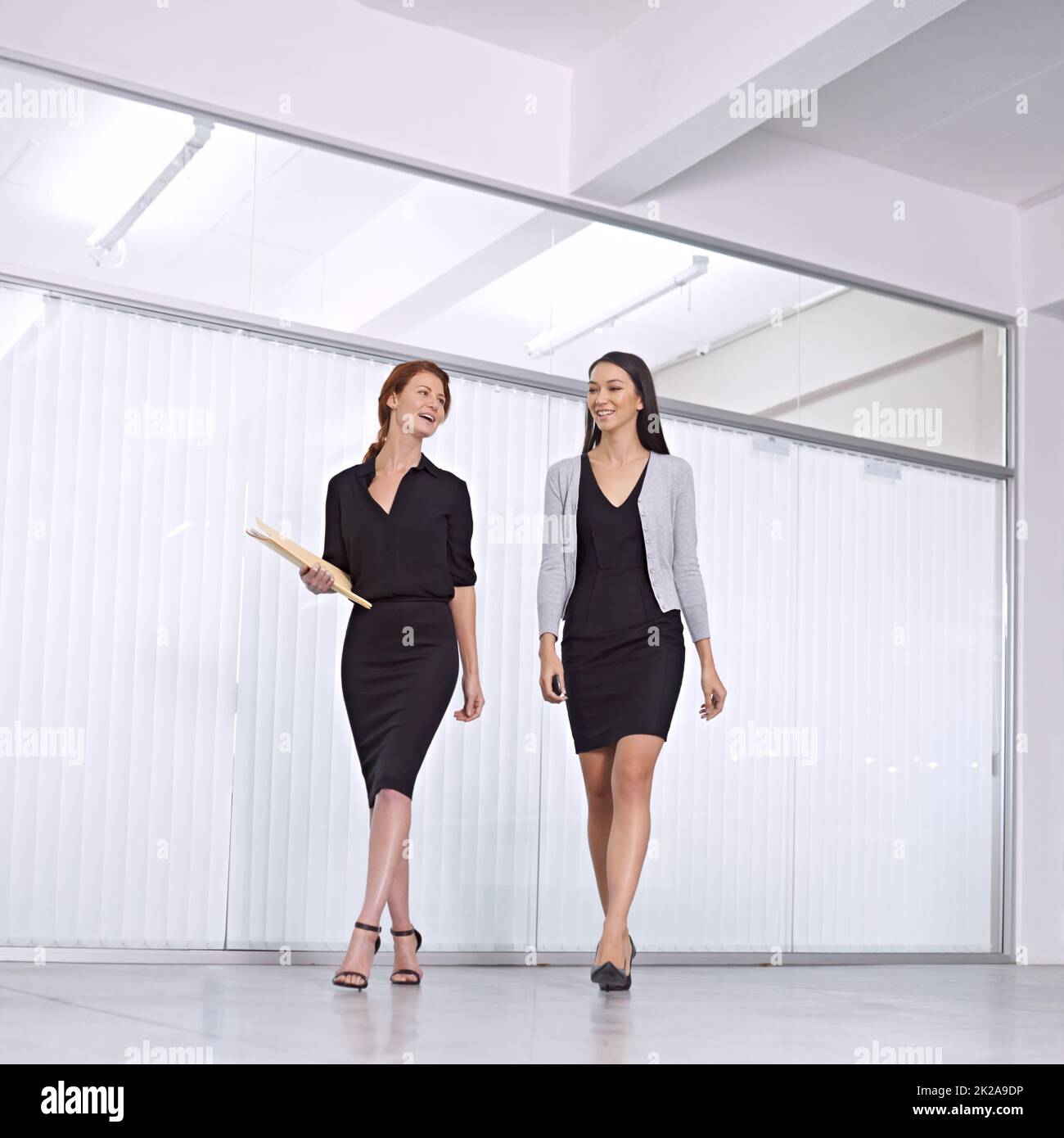 Off to the next meeting. Two colleagues walking together in the office talking. Stock Photo