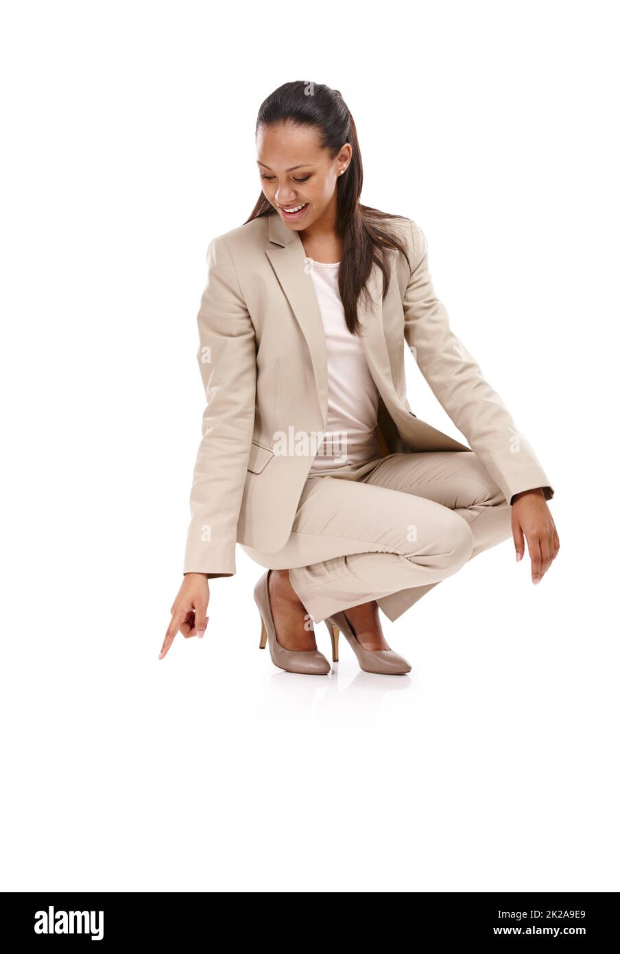 Nowhere to go but up. Full length shot of an attractive young woman in a suit crouching down and pointing towards the ground isolated on white. Stock Photo