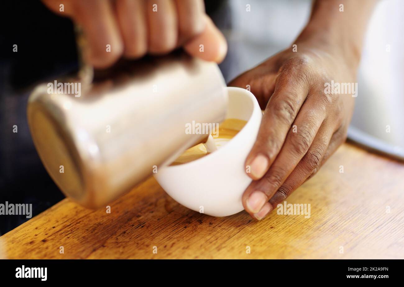 Topping off your cappuccino. Cropped shot of a barista pouring milk froth into a cappuccino. Stock Photo
