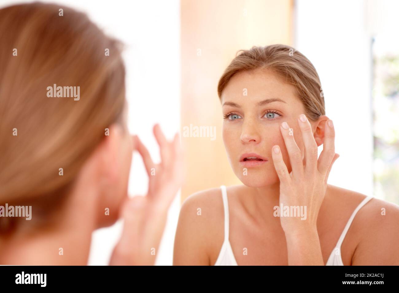 Taking care of her skin. A naturally gorgeous woman applying moisturizing cream in a mirror. Stock Photo