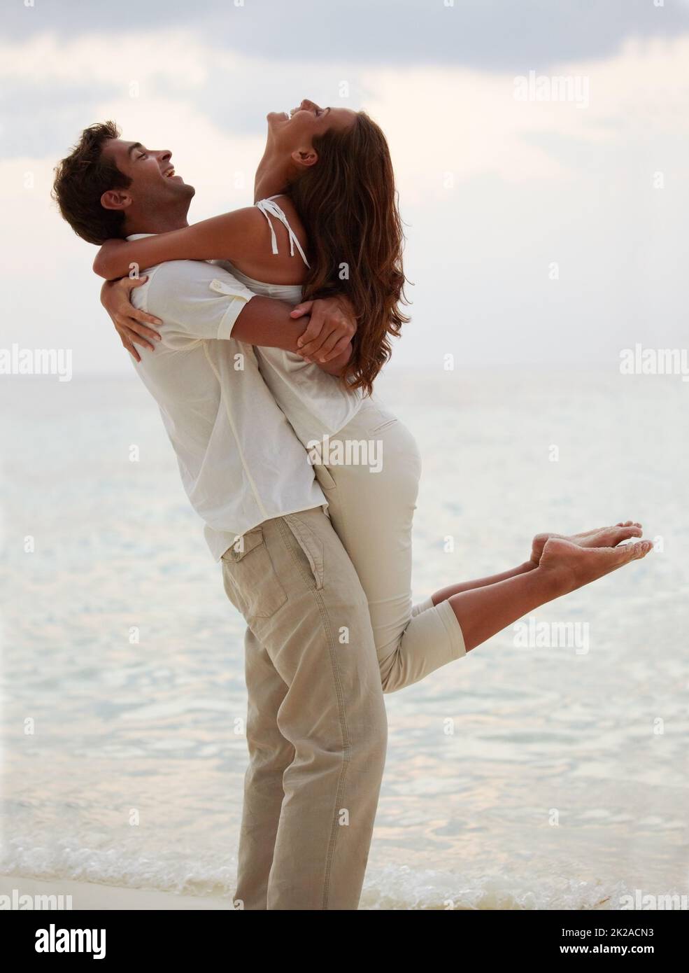 An evening embrace - Romance. Young man lifting his gorgeous girlfriend into the air while on the beach. Stock Photo