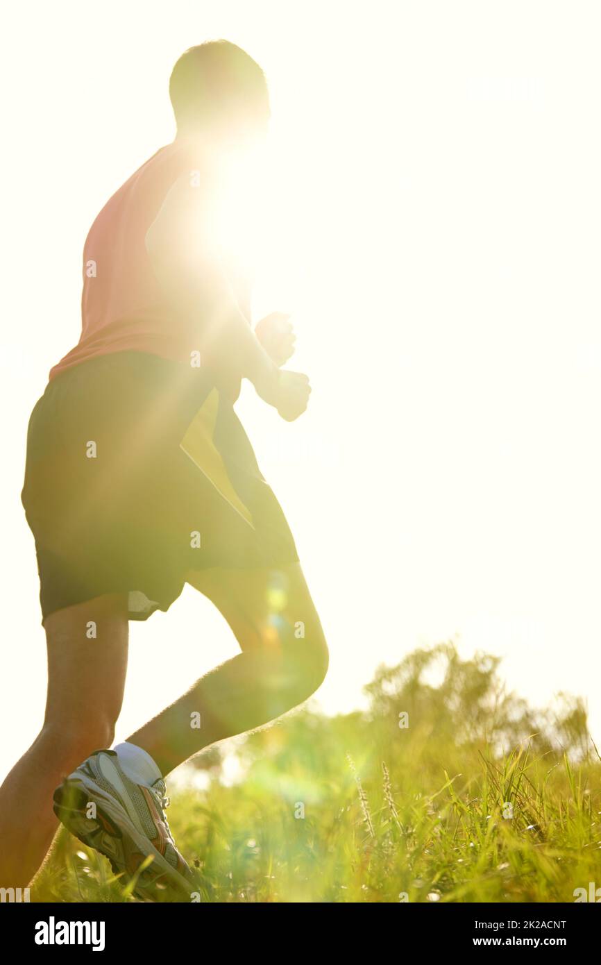 Running in the sunlight. Rearview shot of a young man running outdoors on a mountain trail. Stock Photo