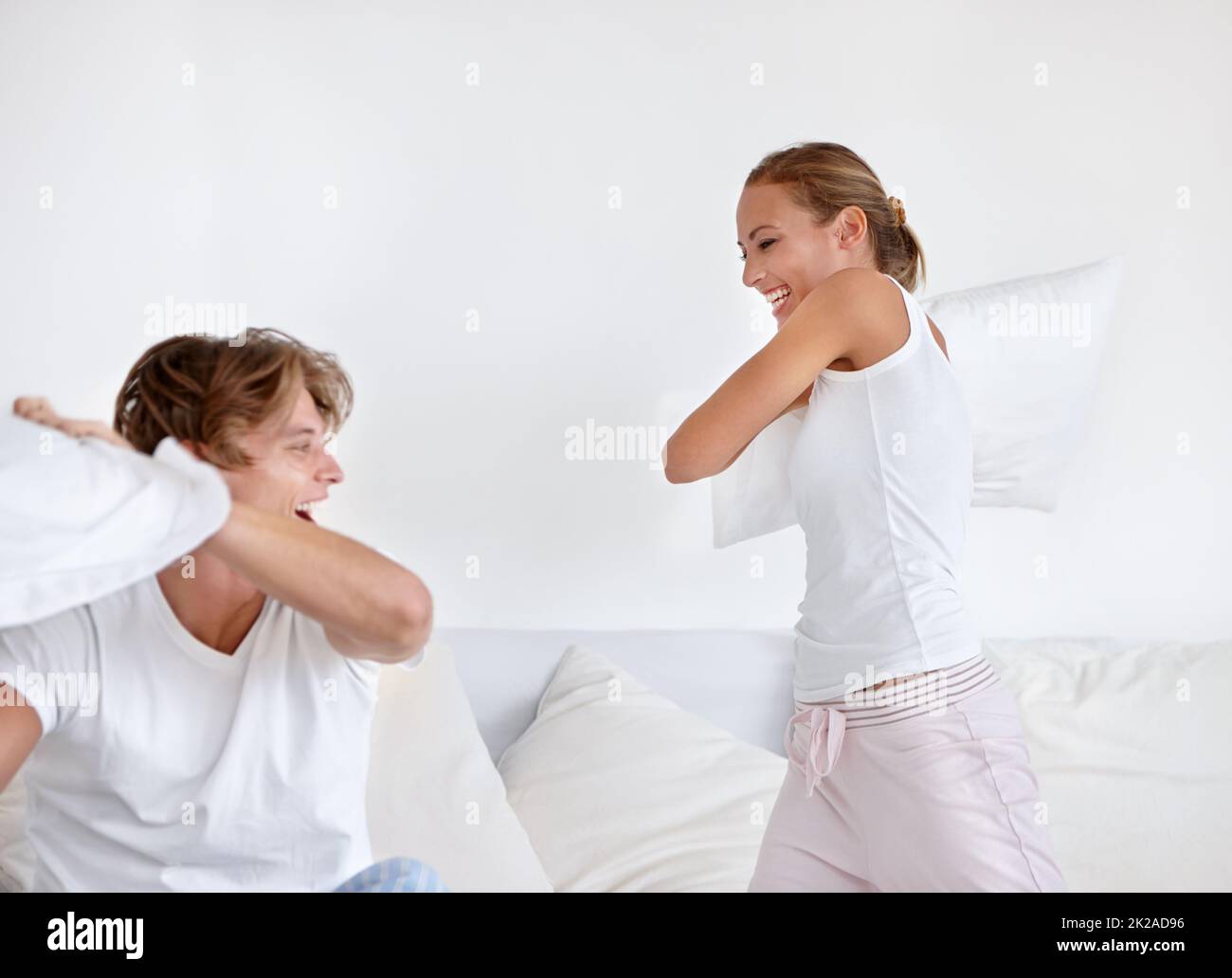 Im gonna get you this time. A young couple wearing pajamas and having a pillow fight together. Stock Photo