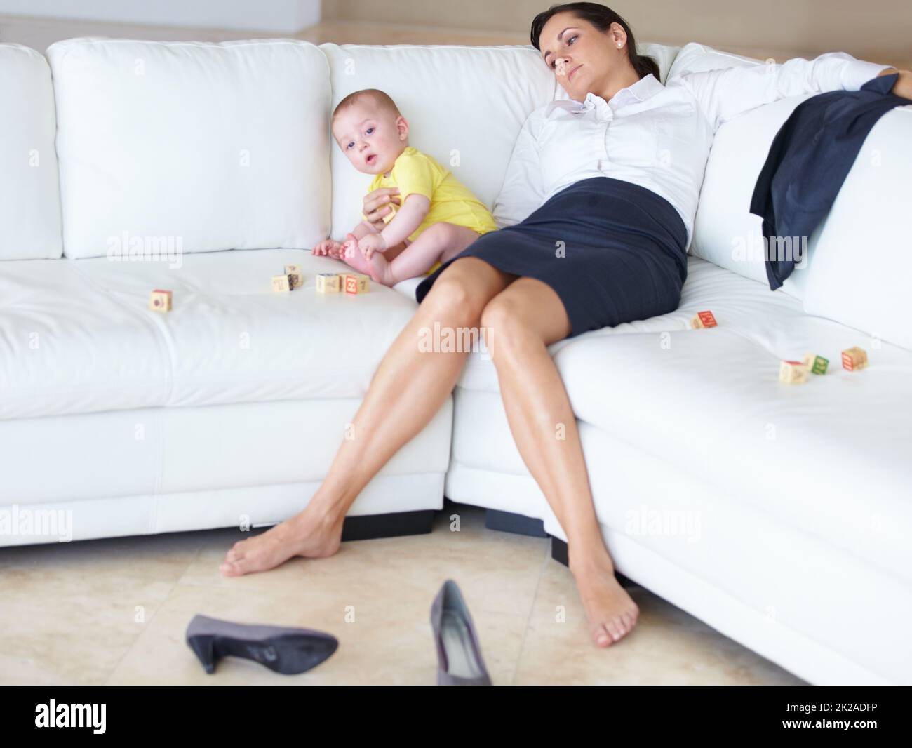 Its tough being a working mom. Exhausted young working mother asleep on the couch next to her baby. Stock Photo