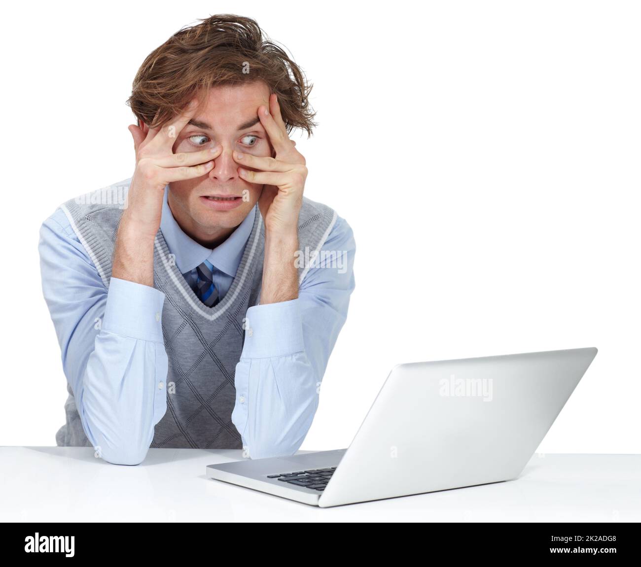 Im freakin out. A young man grimacing through his fingers while sitting next to his laptop. Stock Photo