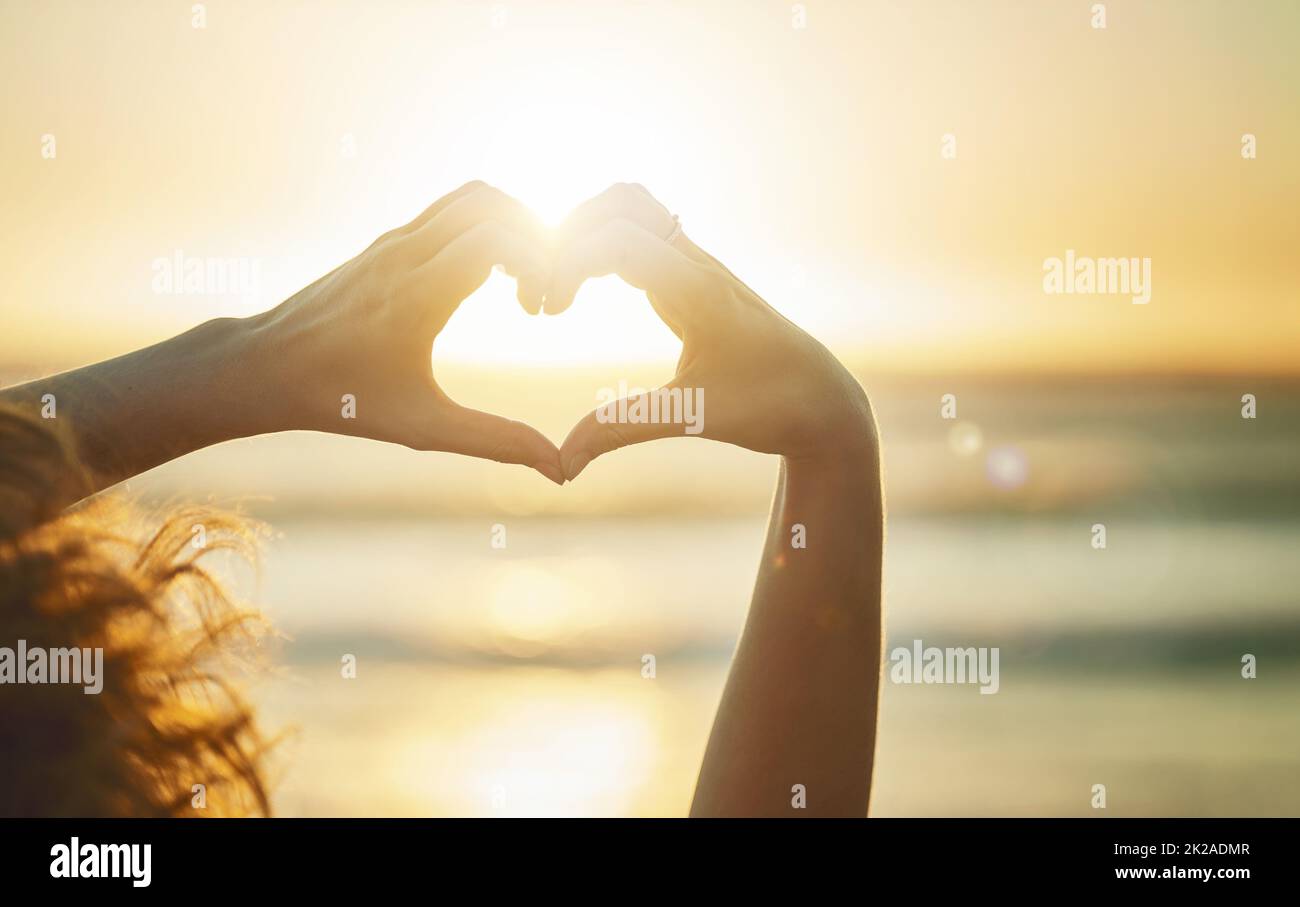 Gotta love summer. Closeup shot of an unidentifiable woman forming a heart shape with her hands at the beach. Stock Photo