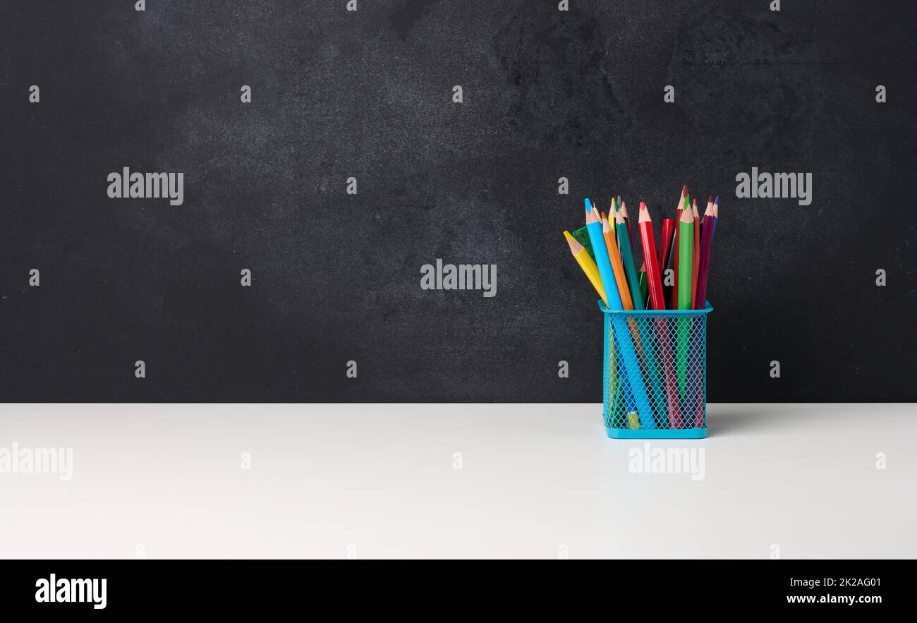 metal glass with pens, pencils and felt-tip pens and scissors on the background of an empty black chalk board, white table Stock Photo