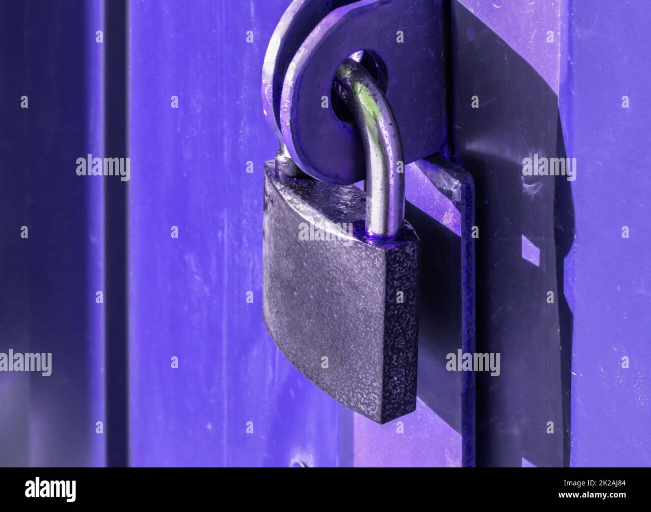 Close-up padlock on the gate of a metal fence made of modern siding, at night, security concept Stock Photo