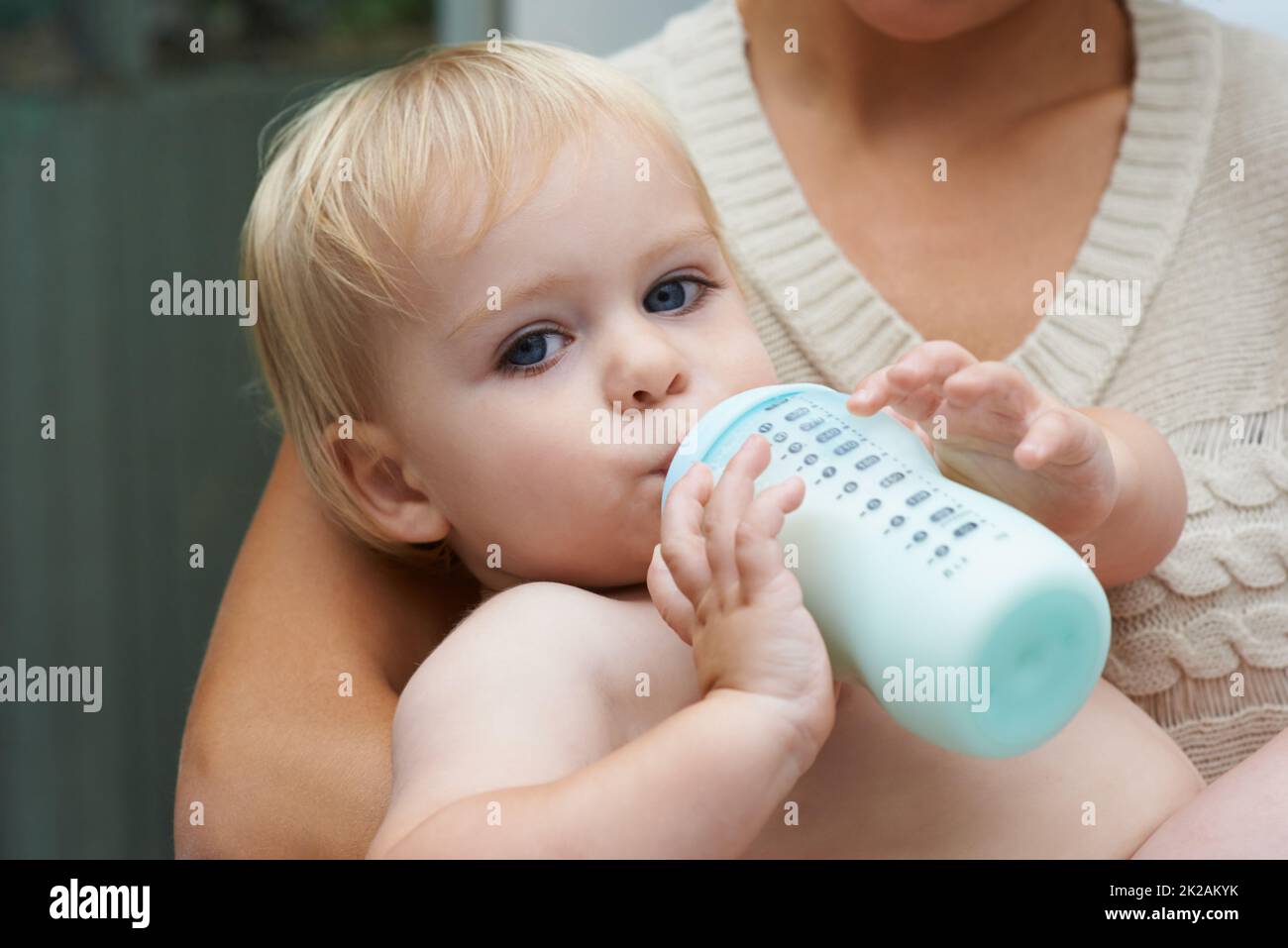 Safe in his mothers arms. A baby boy drinking milk from his bottle while being held by his mother. Stock Photo