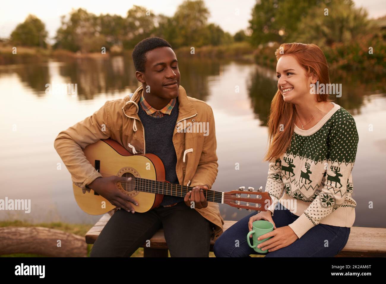 Making her blush. Shot of a teenage boy serenading a beautiful girl while sitting beside a lake. Stock Photo