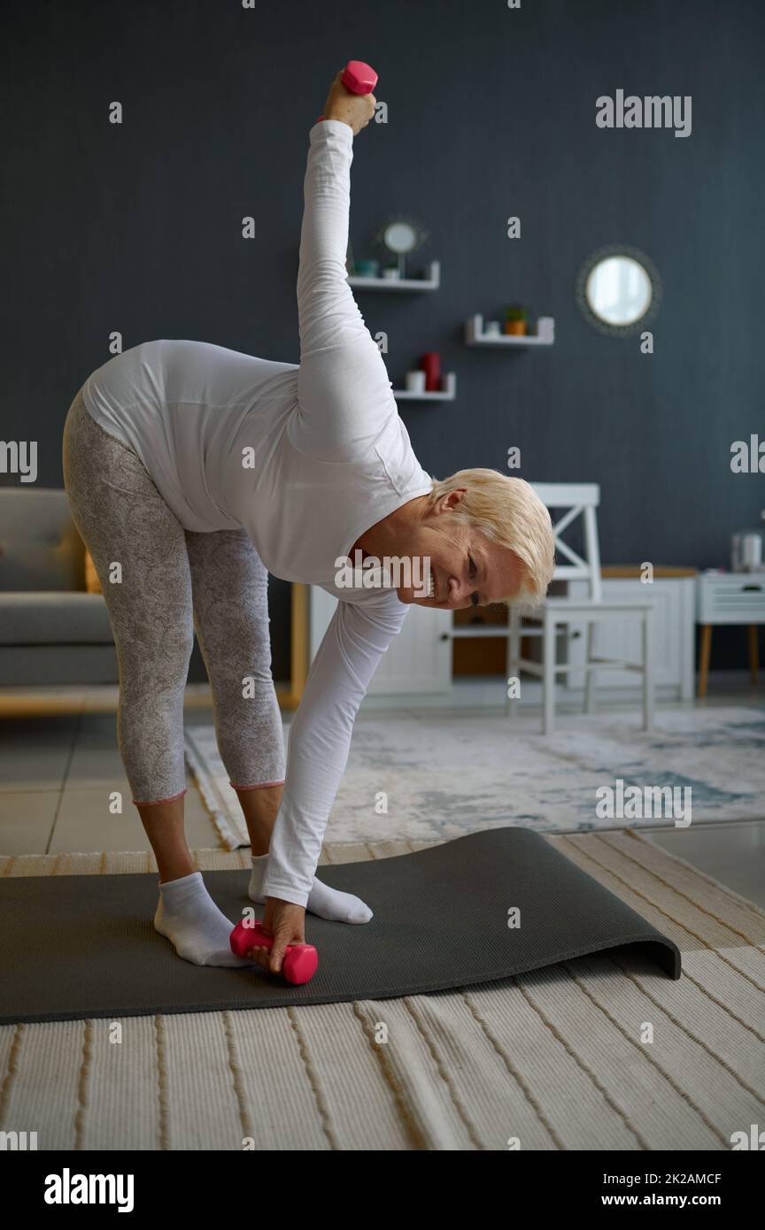 Mature lady exercising with dumbbells at home Stock Photo