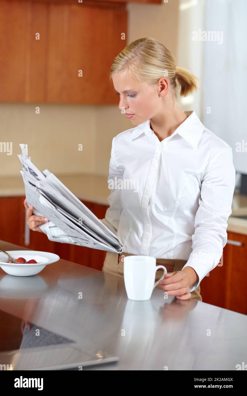 Enjoying her morning routine. A pretty young professional reading the morning paper while enjoying coffee and breakfast. Stock Photo