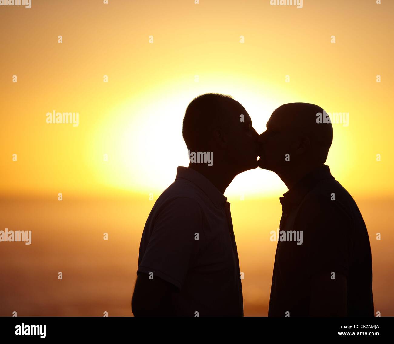 Blissful sunset kiss - Gay Couple. Sihlouette portrait of homosexual couple kissing in front of a sunset - copyspace. Stock Photo